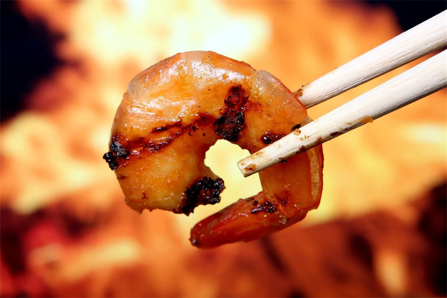 Grilled shrimp held by wooden chopsticks with fiery background